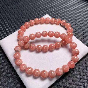 Könnte beinhalten: Zwei rosafarbene und weiße gestreifte Edelstein-Armbänder. Die Armbänder bestehen aus runden Perlen und sind übereinander gestapelt.