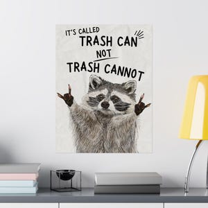 May include: A raccoon with a mischievous expression is holding up its paws in a rock and roll hand gesture. The text "It's called Trash Can not Trash Cannot" is written in black on a white background.