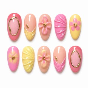 May include: A collection of ten artificial nails in various designs. The nails feature a range of colors, including pink, yellow, and peach, with gold accents and floral or textured patterns. The nails are oval-shaped.