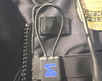 May include: A black square-shaped device with a blue "S" logo attached to a black strap. The device is worn on a black vest.