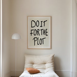 Può includere: Interno di un soggiorno con una poltrona color crema e un cuscino arancione. Una stampa incorniciata con la scritta "DO IT FOR THE PLOT" è appesa al muro. Una lampada da terra bianca e pavimenti in legno completano la scena.