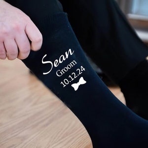 Puede incluir: Calcetines negros de vestir con texto blanco que dice "Sean Groom 10.12.24" y un gr&aacute;fico de pajarita.