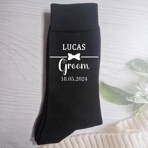 Puede incluir: Calcetines negros con texto blanco que dice "Lucas Groom 18.05.2024" con un gr&aacute;fico de pajarita.