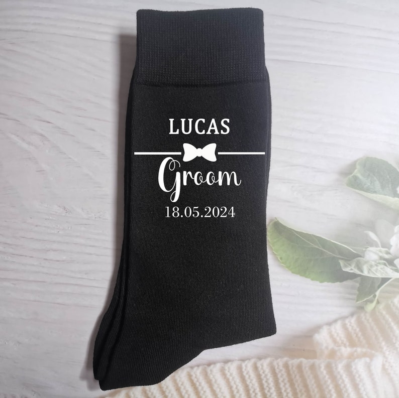 Puede incluir: Calcetines negros con texto blanco que dice "Lucas Groom 18.05.2024" con un gr&aacute;fico de pajarita.