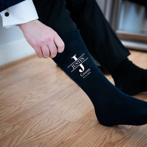 Puede incluir: Calcetines negros de vestir con un dise&ntilde;o blanco que incluye la letra "J" y el texto "Justin Groom 01.12.2023".