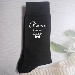 Puede incluir: Calcetines negros con texto blanco que dice "Kevin Groom 10.12.24" y un gr&aacute;fico de pajarita.
