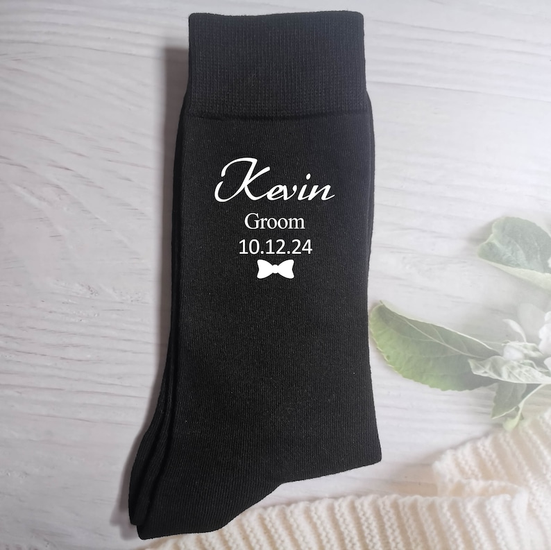Puede incluir: Calcetines negros con texto blanco que dice "Kevin Groom 10.12.24" y un gr&aacute;fico de pajarita.
