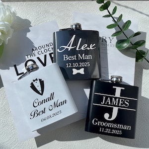 May include: Three personalised stainless steel hip flasks with different designs. The first flask is white with black text that reads "Conall Best Man 04.08.2025" and a tuxedo graphic. The second flask is black with white text that reads "Alex Best Man 12.10.2025" and a bowtie graphic. The third flask is black with white text that reads "JAMES J Groomsman 11.22.2025".