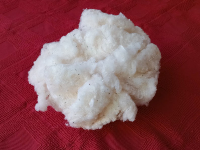 May include: A large clump of white cotton fibers, likely raw cotton, on a red background.
