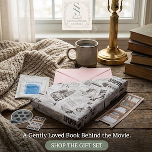 May include: A cozy scene with a wrapped gift, coffee mug, and books. The gift is wrapped in newspaper print. A pink envelope and a packet of Swiss Miss are also present. The text reads "A Gently Loved Book Behind the Movie."
