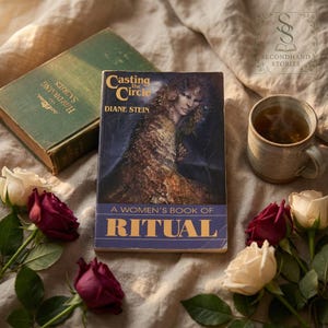 Può includere: Una natura morta con un libro intitolato "Casting the Circle" di Diane Stein, sottotitolato "A Women's Book of Ritual". Un libro verde vintage, rose e una tazza di tè completano la scena. La copertina del libro presenta un ritratto di donna.