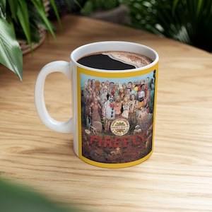 May include: White ceramic mug with a yellow band around the top. The mug features a colorful illustration of a group of people with the text "Firefly" and "The Devil's Rejects" on the front.