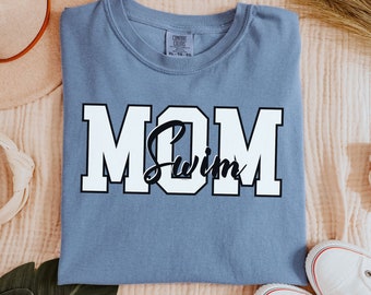 Puede incluir: Una camiseta azul claro con el texto "MOM Swim" en letras blancas en bloque con un contorno negro.