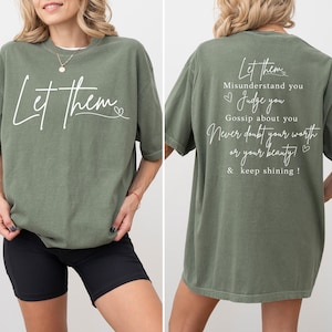 May include: An olive green t-shirt with the words "Let them" in a cursive font on the front. The back of the shirt has the text "Let them misunderstand you, judge you, gossip about you, never doubt your worth or your beauty & keep shining!"