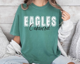 Puede incluir: Una camiseta verde azulada con las palabras "Eagles Oakwood" impresas en blanco y negro. El texto está en un estilo vintage y desgastado.