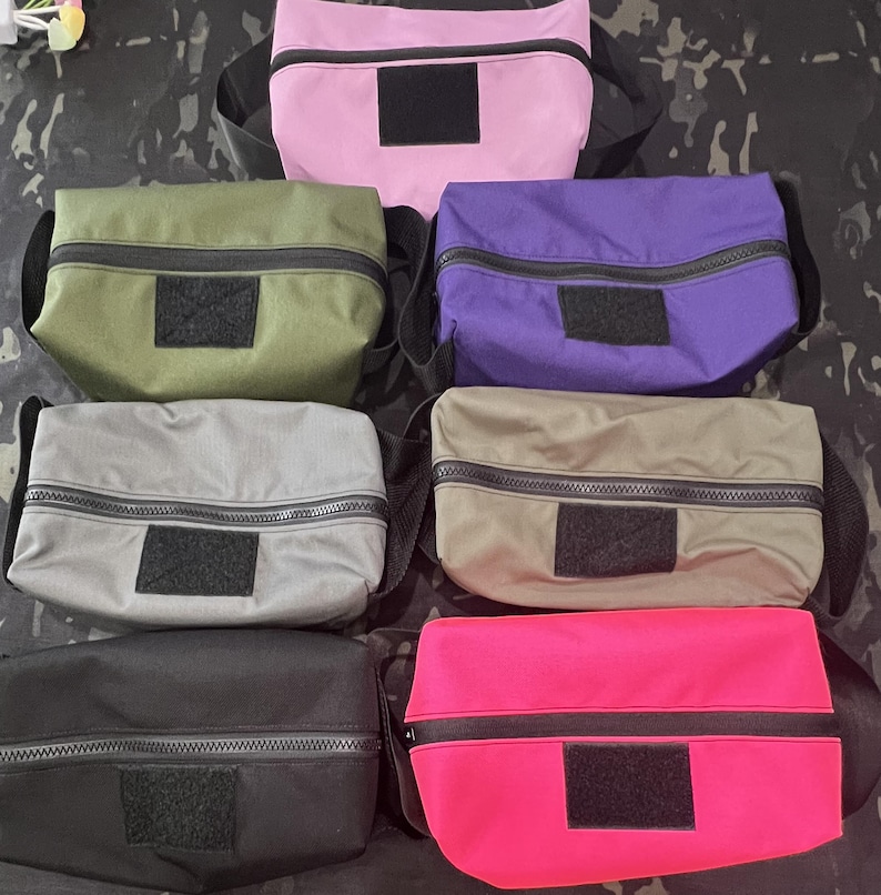 Puede incluir: Seis bolsas con cremallera de diferentes colores, incluyendo rosa, verde, morado, gris, negro y rosa brillante. Cada bolsa tiene un parche de velcro negro en la parte delantera.