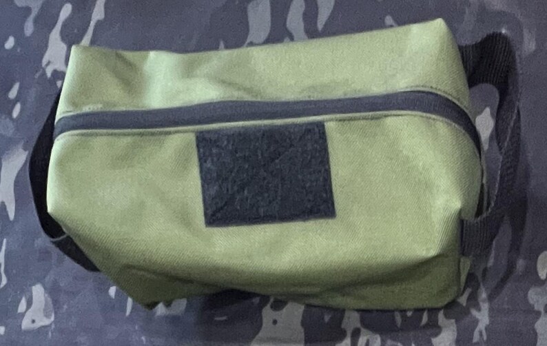 Puede incluir: Una bolsa de lona verde con cremallera, una correa negra y un parche de velcro negro.