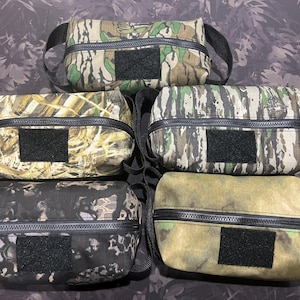 May include: Five camouflage-patterned zippered pouches with black straps and black velcro patches. The pouches are made of a durable fabric and are perfect for storing small items.
