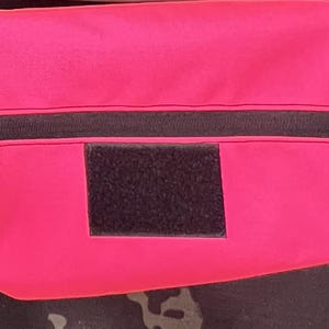 Puede incluir: Una bolsa de color rosa brillante con una cremallera negra y un parche de velcro negro. La bolsa est&aacute; hecha de un material suave y duradero y tiene una correa para llevar.