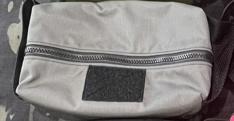 Puede incluir: Una bolsa gris con cremallera y un parche de velcro negro. La bolsa est&aacute; hecha de un material resistente al agua.