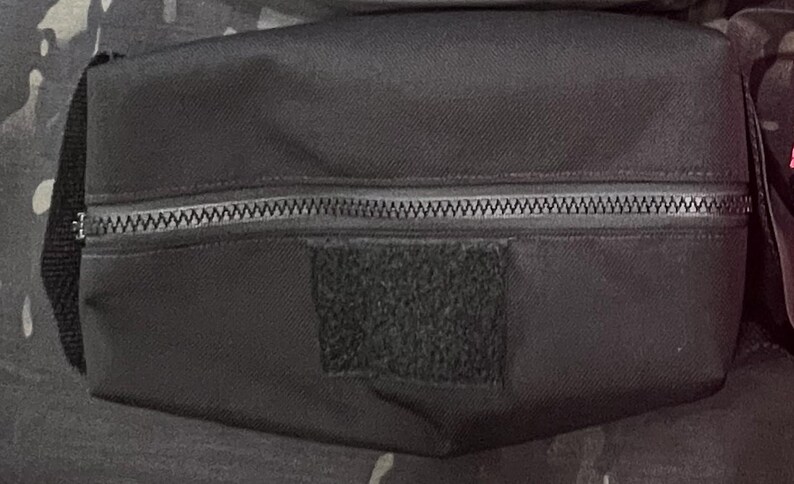 Puede incluir: Una bolsa negra con cremallera y un parche de velcro negro. La bolsa est&aacute; hecha de un tejido resistente y tiene un cierre de cremallera.