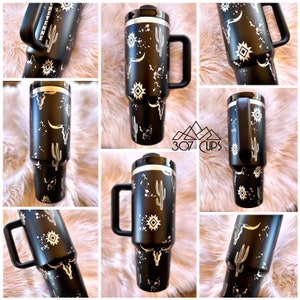 May include: Black and silver stainless steel travel mug with a western design featuring a cactus, a skull, and a southwestern pattern. The mug has a black handle and a silver lid.