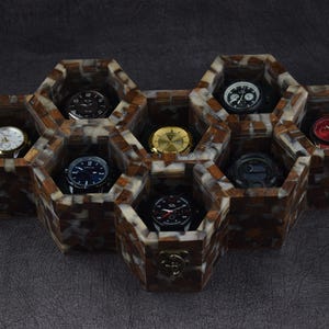 May include: A honeycomb-shaped watch storage organizer constructed from brown and white marbled resin. The unit features seven individual hexagonal compartments, each containing a different wristwatch with various dial colors including black, white, gold, and red.