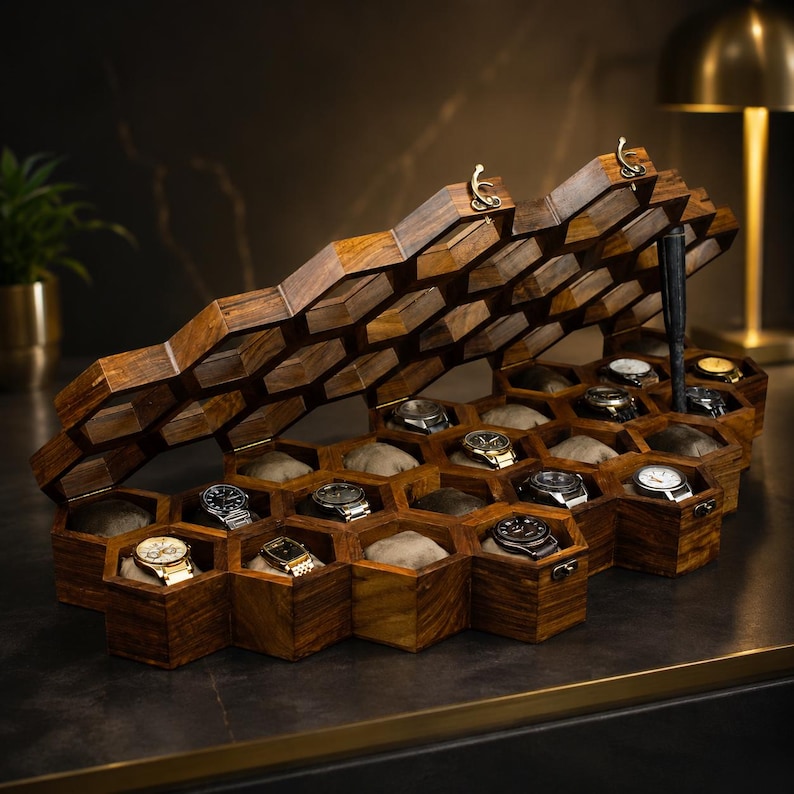 Puede incluir: Un estuche de madera de color marr&oacute;n oscuro para relojes con una estructura en forma de panal. La caja cuenta con m&uacute;ltiples compartimentos hexagonales, cada uno con un reloj sobre un coj&iacute;n beige. La tapa tiene bisagras y est&aacute; abierta.