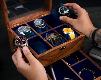 May include: A wooden watch box with a glass lid and blue velvet interior, featuring multiple compartments for watches, a lower drawer for accessories, a metal latch, and various wristwatches with different colored straps and dials.