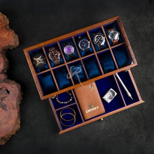 May include: A rectangular wooden storage box with a hinged lid and a pull-out drawer, featuring blue velvet lining. The top section holds five wristwatches, while the drawer contains a tan leather wallet, a metal lighter, a pen, and jewelry.
