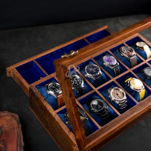May include: A rectangular wooden watch display case with a hinged glass lid and a brass latch. The interior features multiple compartments lined with vibrant blue velvet, each containing a wristwatch resting on a soft cushion for storage.