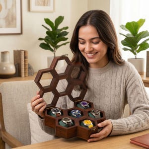 Puede incluir: Un estuche de madera de color marr&oacute;n oscuro para relojes con forma de panal y tapa abatible. El interior cuenta con seis compartimentos individuales, cada uno con un reloj de pulsera sobre un coj&iacute;n de terciopelo verde.