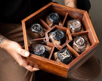May include: A wooden watch display case with seven compartments, each holding a wristwatch. The watches have various band and face designs. The case is held by a person.