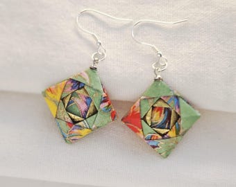 May include: A pair of origami earrings. Each earring has a diamond-shaped design with a green border and a colourful, patterned interior. The earrings have silver-coloured fish hook ear wires. The earrings are displayed on a white surface.