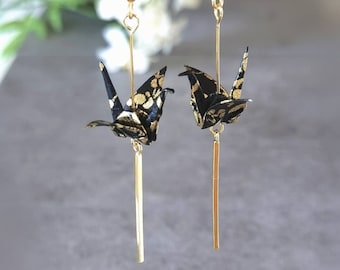 May include: A pair of gold dangle earrings featuring black origami cranes with gold accents. The cranes are suspended from gold chains with gold hooks.
