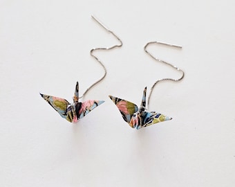 May include: A pair of silver dangle earrings featuring origami cranes made of patterned fabric. The cranes are blue, pink, and green with black accents.