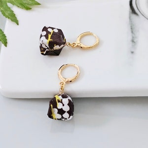 May include: A pair of gold hoop earrings with a brown and white patterned charm hanging from each hoop.