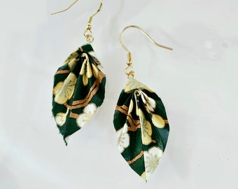 May include: A pair of leaf-shaped earrings. The earrings are made of dark green paper with gold and white floral patterns. They hang from gold-colored ear wires, creating a delicate and artistic accessory.