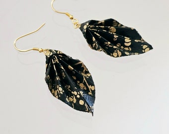 May include: A pair of black and gold leaf-shaped earrings. The earrings are made of fabric with a gold floral pattern.