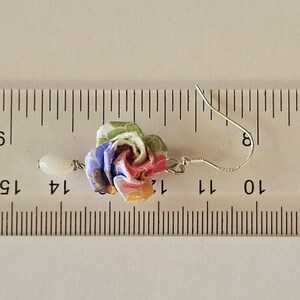 May include: A fabric rose earring with a white bead drop. The rose is made of pink, blue, yellow, and green fabric. The earring, including the hook, is approximately 3.2 cm long.