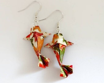 May include: A pair of origami fish earrings with a red, orange, green and white floral pattern. The earrings are made of paper and have silver hooks.