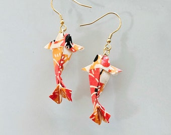 May include: A pair of origami koi carp earrings. The fish are made of patterned paper in shades of red, orange, and white, with black accents. The earrings have gold-coloured fish hooks.