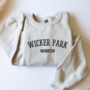 May include: A beige sweatshirt with black text that reads "Wicker Park Chicago" in a collegiate font.
