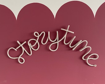 Puede incluir: Una decoración de pared de cuerda blanca con la palabra "Storytime" en una pared burdeos con un borde blanco festoneado.