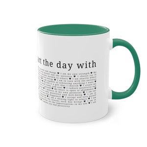 Pode incluir: Caneca de café de cerâmica branca com borda e alça verdes. A caneca apresenta um design de texto preto e branco que diz "Start the day with..." e inclui uma série de corações e citações inspiradoras.