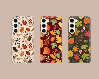 May include: Three phone cases with different autumn leaf patterns. The first case has a white background with orange, red, and brown leaves. The second case has a dark red background with orange, yellow, and brown leaves. The third case has a dark green background with orange, yellow, and brown leaves.