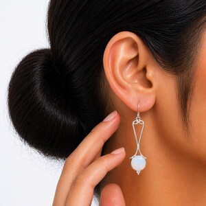 Peut inclure: Boucles d'oreilles pendantes en argent avec un design en forme de goutte d'eau et une pierre précieuse blanche et ronde. Les boucles d'oreilles ont un dessus décoratif avec un petit crochet pour l'oreille.