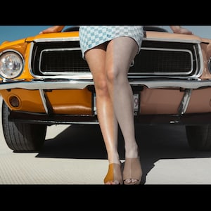 Pu&ograve; includere: Un'auto d'epoca arancione e beige con dettagli cromati. Una persona &egrave; in piedi davanti all'auto, con una gonna a scacchi e tacchi marroni e beige. L'auto &egrave; un classico.