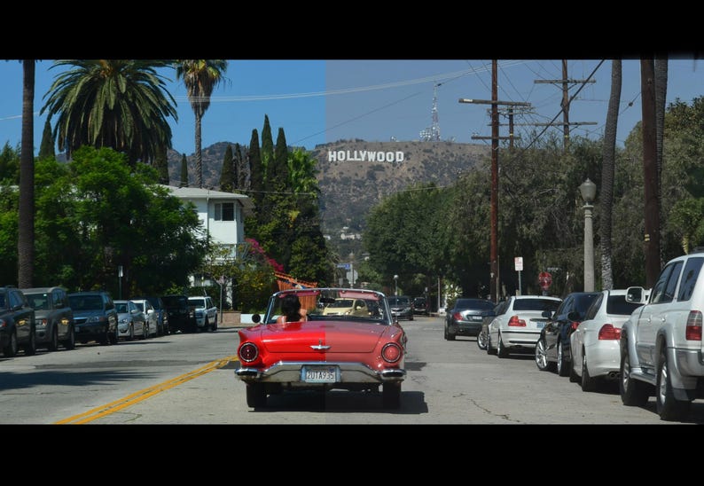 May include: A red vintage convertible car drives down a street lined with parked cars and palm trees. The Hollywood sign is visible on a distant hillside under a blue sky.