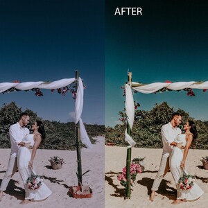 May include: A couple in white clothing stand under a white fabric canopy decorated with pink flowers, on a sandy beach. The couple is smiling and looking at each other. The sky is blue.